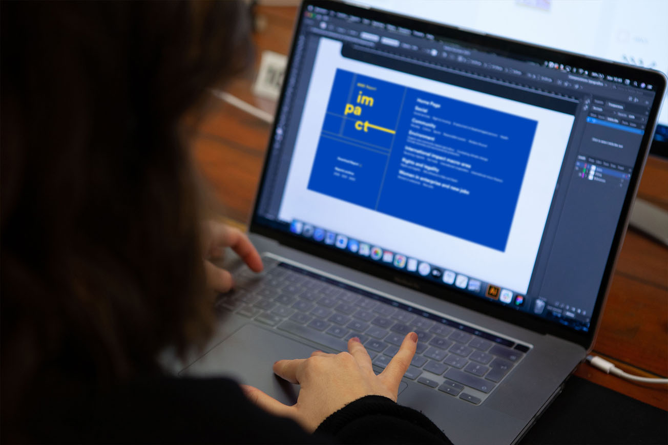 A person works on a laptop, displaying a graphic design with the word "impact" on a blue background.