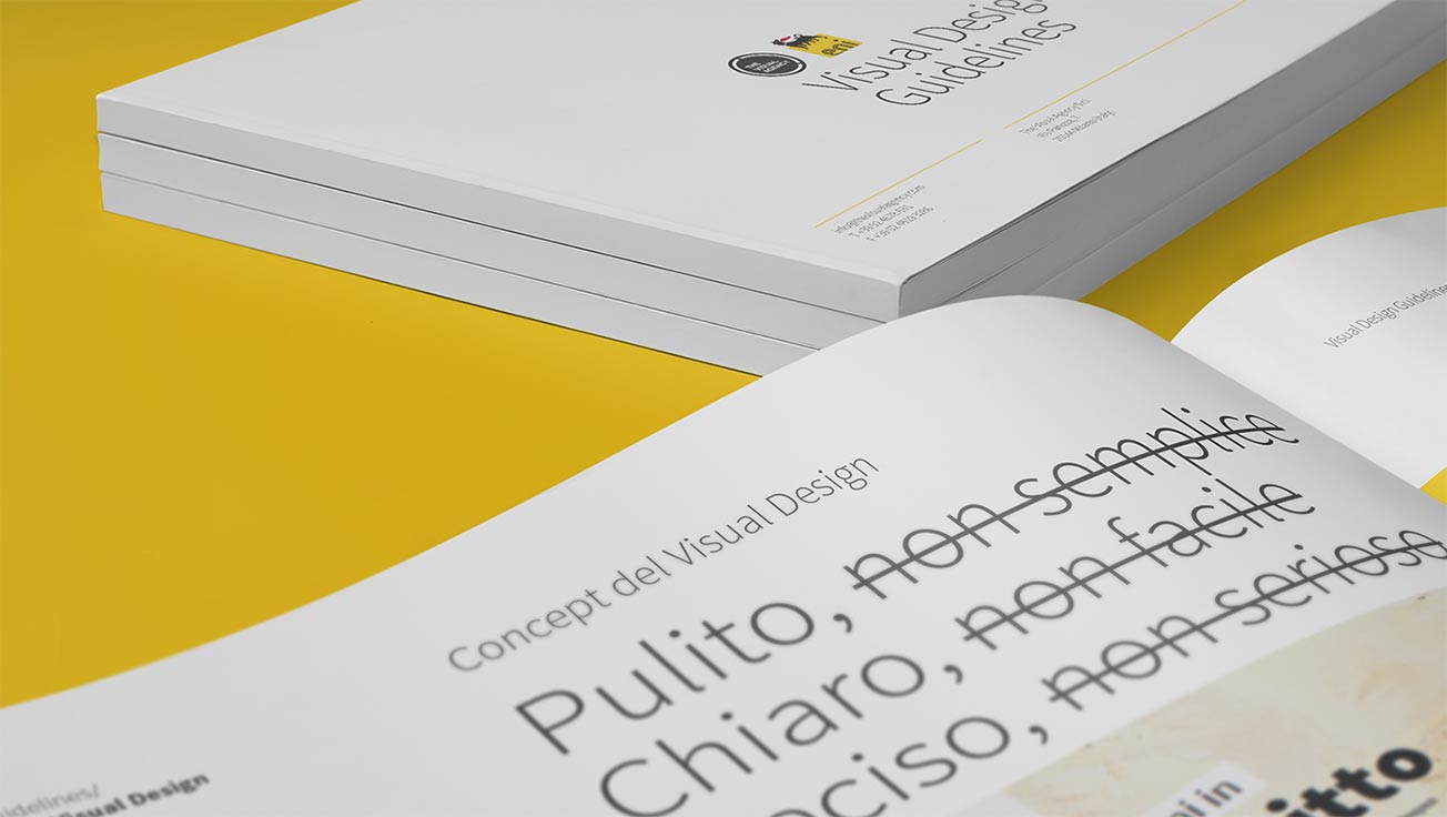 An open Visual Design Guidelines book with Italian text, partially revealing a stack of similar books on a yellow surface.