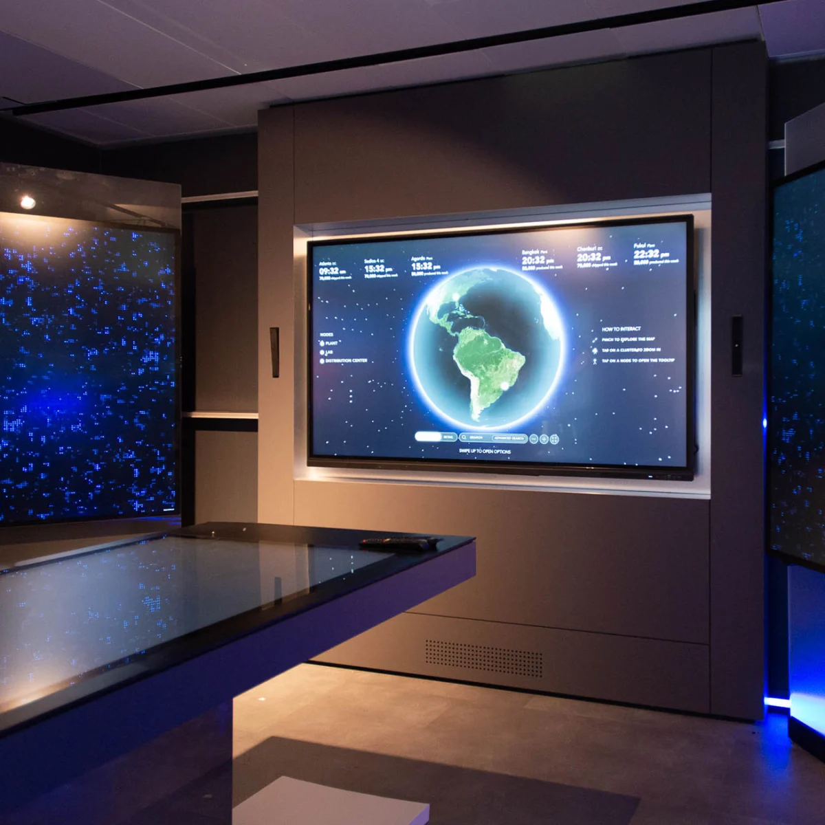 A large screen in a dark room displays a digital globe with time zone information and other interactive elements